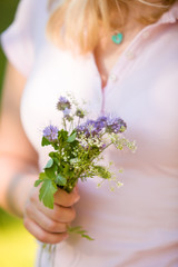 Young blond woman in pink holding a beautiful garden flowers in her hand. Summer bouquet in girl's hand. Outdoor. Spring garden present. Person with bunch of flowers.
