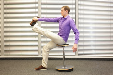man stretching leg,sitting on pneumatic stool  in office - healthy lifestyle, profile view