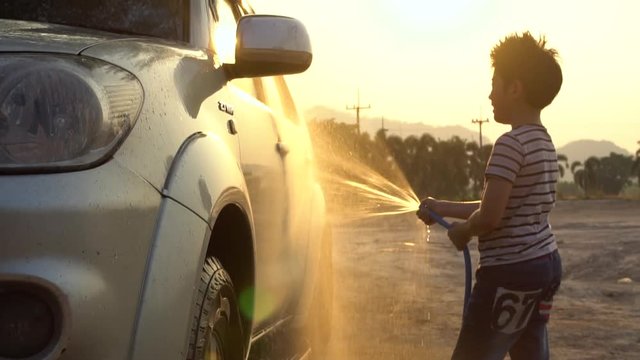 Happy asian kid washing car with water spray .Slow motion shoot with sunset and flare ,120 Fps By Sony A6300