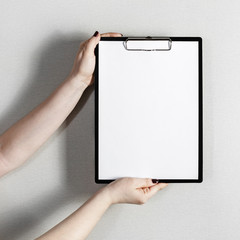 Blank paper poster in female hands. Clipboard with a blank paper. Mock-up for graphic designers portfolios.