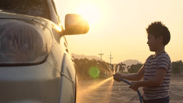 Happy asian kid washing car with water spray .Slow motion shoot with sunset and flare ,120 Fps By Sony A6300
