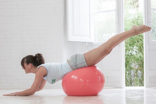 Young Woman Exercising On Pink Exercise Ball At Home