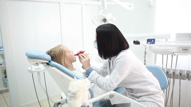 Young handsome dentist treats tooth girl child in dentistry.