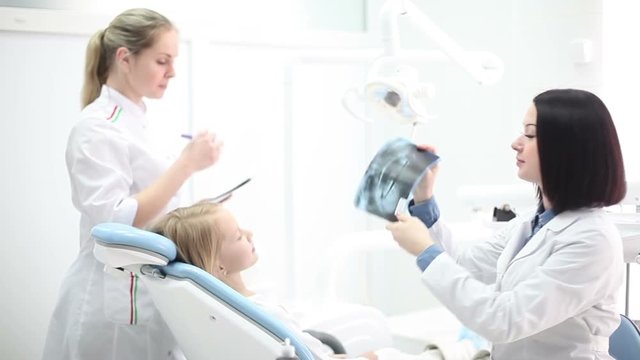 Young beautiful girl dentists examine x-ray of the patient and prepare for tooth treatment.