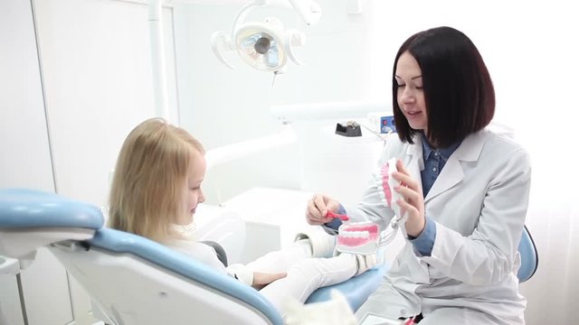 Young beautiful woman dentist shows a child how to properly brush their teeth.