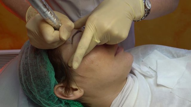 Cosmetologist making permanent makeup eyebrow