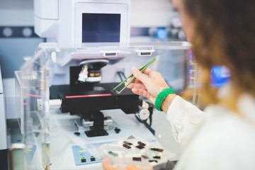 Female scientist using FTIR spectrophotometer, positioning thin film sample on microscope stage