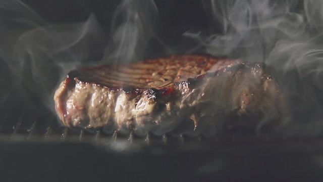 SLOW: A steak of meat is cooking on a grill
