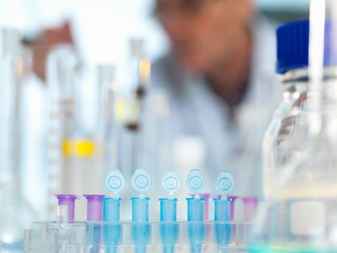 Row of eppendorf vial awaiting sample for testing in laboratory, scientist out of focus in background