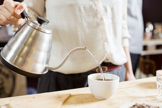 Coffee taster pouring hot water into cup of coffee