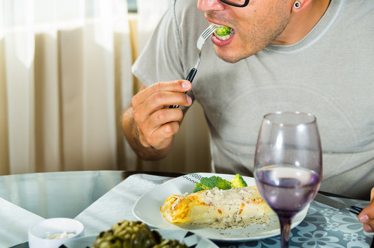 Man Sitting By Classy Dinner Setting Eating Fork With Broccoli, Crepe Covered In White Sauce Lying On Plate