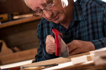 Senior carpenter working in his workshop. He is cutting wooden plank with handsaw.