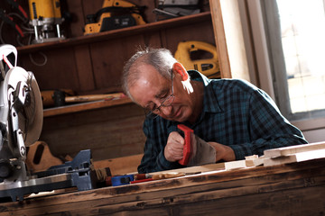 Senior carpenter working in his workshop. He is cutting wooden plank with handsaw.