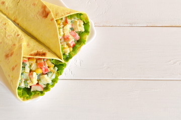 Pita bread with corn, eggs, crab meat, green onion, leaf of lettuce. White wooden background with empty place for text
