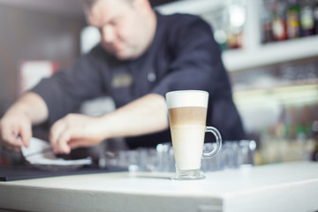 Fototapeta na wymiar Barista prepares cappuccino in his coffee shop. Close-up cup of coffee.