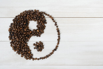 Top view of coffee beans making a symbol Yin yang on light wooden surface - Powered by Adobe