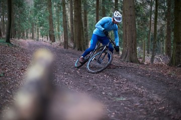 Cyclist on tree lined dirt track wearing cycling helmet falling off bicycle