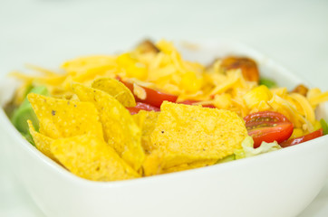 Closeup mexican salad in white bowl, yellow tortilla chips and tomatoes visible