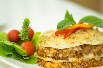 Closeup elegant serving of lasagne and small salad sitting on white plate