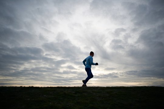 Low angle full length side view of runner against dramatic sky