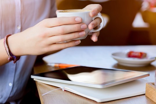 Hands of young woman holding coffee cup using digital tablet