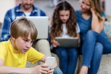 Boy using a mobile phone while family in background