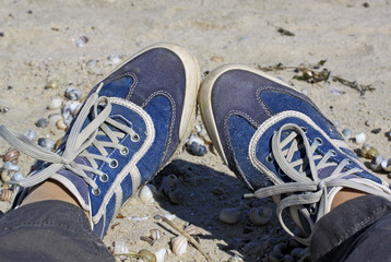 Female legs in jeans blue sneakers in the background of the sand