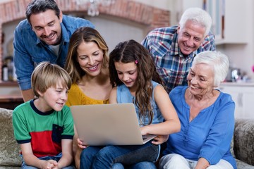 Fototapeta na wymiar Multi-generation family sitting on sofa and using laptop