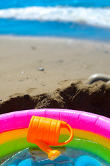 Summer vacation on the beach. Rainbow Children's inflatable pool with water and watering on the beach.