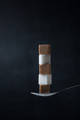 Pyramid of white and brown sugar cubes in a teaspoon on a dark background.