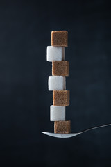 Pyramid of white and brown sugar cubes in a teaspoon on a dark background.