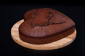 Chocolate cake on light wooden cutting board on black background