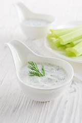 Fresh celery sticks with yogurt dip on white wooden background
