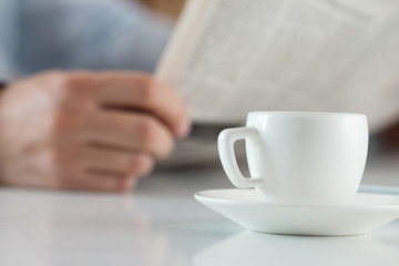 Cup of morning coffee on worktable with businessman reading news