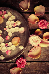 Pink and yellow rose petals in silver bowl with water on wooden background