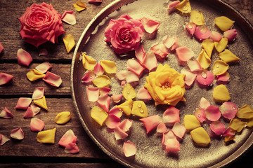 Naklejka na ściany i meble Pink and yellow rose petals in silver bowl with water on wooden background