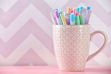 Pens in ceramic cup, pencils and markers on color background