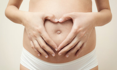 Heart shaped hands of pregnant woman on her belly