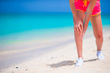 Female athlete suffering from pain in leg while exercising on white beach