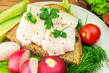 Sandwich with slice of rye bread, fresh pork lard and parsley in the plate, fresh produce, vegetables, close-up.