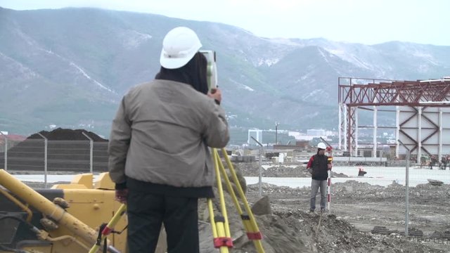 Industrial worker in a protective helmet with tacheometer at the construction site.Engineer using tacheometer or theodolite for survey line columns for the construction of buildings.