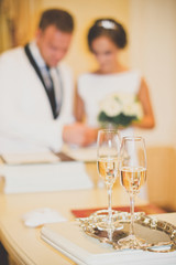 Wedding glasses are in the foreground. Blurred outlines newlywed