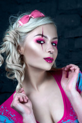 Beautiful blonde girl with two pigtails, with creative doll make-up: pink glossy lips, wearing pink skeleton dress. for the Halloween party. Close up, retouched image.