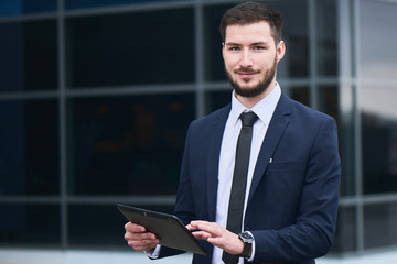 Portrait of businessman with tablet in hand on the background of the building with a glass facade
