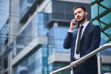 Businessman talking on cell phone holding on to the metal railing on the background of the building...