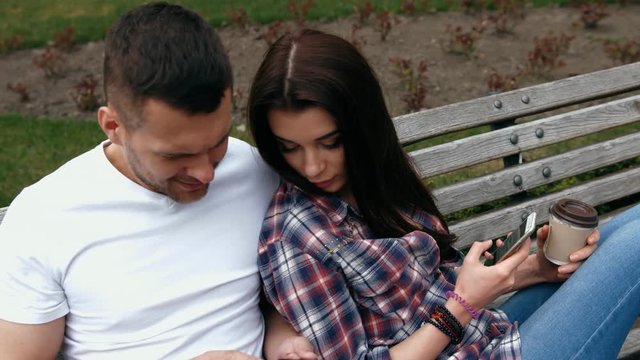 ouple sitting on a bench using mobile phone or digital tablet