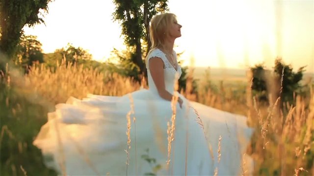 Beautiful blonde bride  in long bridal dress running through the rye field on sunset