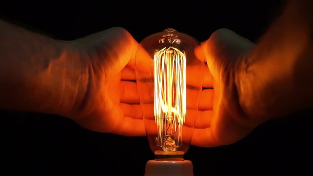 Close up point of view or POV shot of an anonymous man warming his hands with the heat produced by an antique retro style carbon filament bulb.