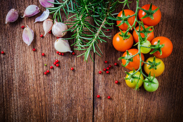 Cherry tomatoes, garlic and rosemary on wooden background