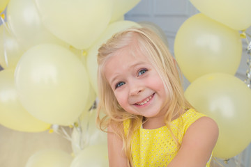 Portrait of a smiling little girl in a yellow dress with a yellow balloons